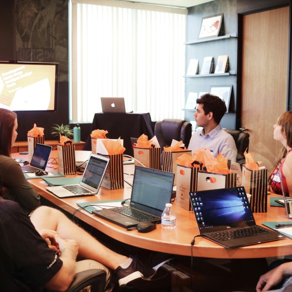 A diverse group of people collaborating around a table, each using a laptop for discussion and teamwork